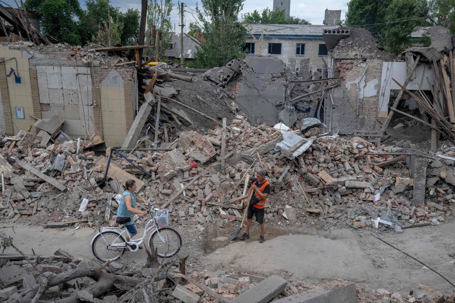 A local resident pushes her bicycle through damaged buildings in Toretsk, eastern Ukraine on August 5, 2022, amid the Russian invasion of Ukraine.