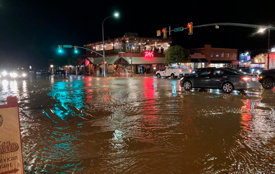 In this photo courtesy of City of Moab, vehicles navigate high waters at the intersection of South Main Street and 100 South in Moab, Utah on Saturday, Aug. 20, 2022. Nearly an inch of rain fell in the area in 20 minutes, leading Mill Creek to overflow and causing flooding of up to 3 feet in depth in places. (Rani Derasary/City of Moab via AP)