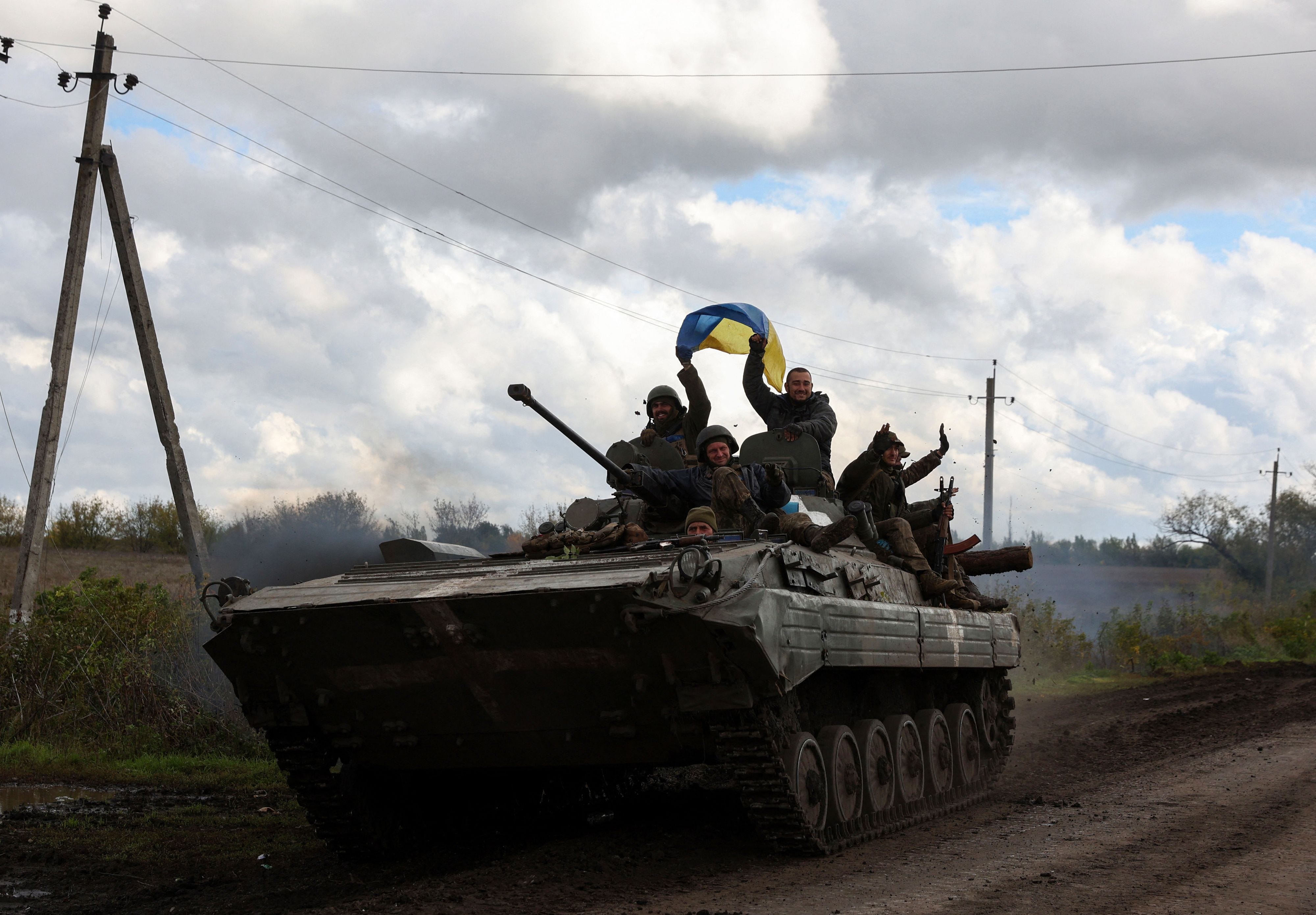 Ukrainian soldiers wave a national flag atop a personnel armoured carrier on a road near Lyman, Donetsk region on October 4, 2022, amid the Russian invasion of Ukraine. (Photo by Anatolii Stepanov / AFP)