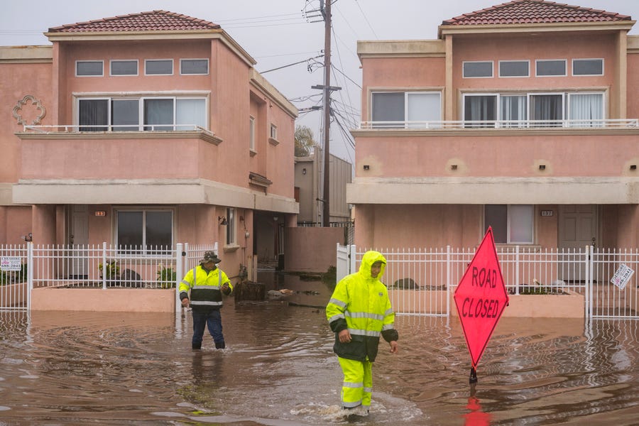 A cleaning crew walks through floodwaters in the Rio Del Mar neighborhood of Aptos, Calif., Monday, Jan. 9, 2023.