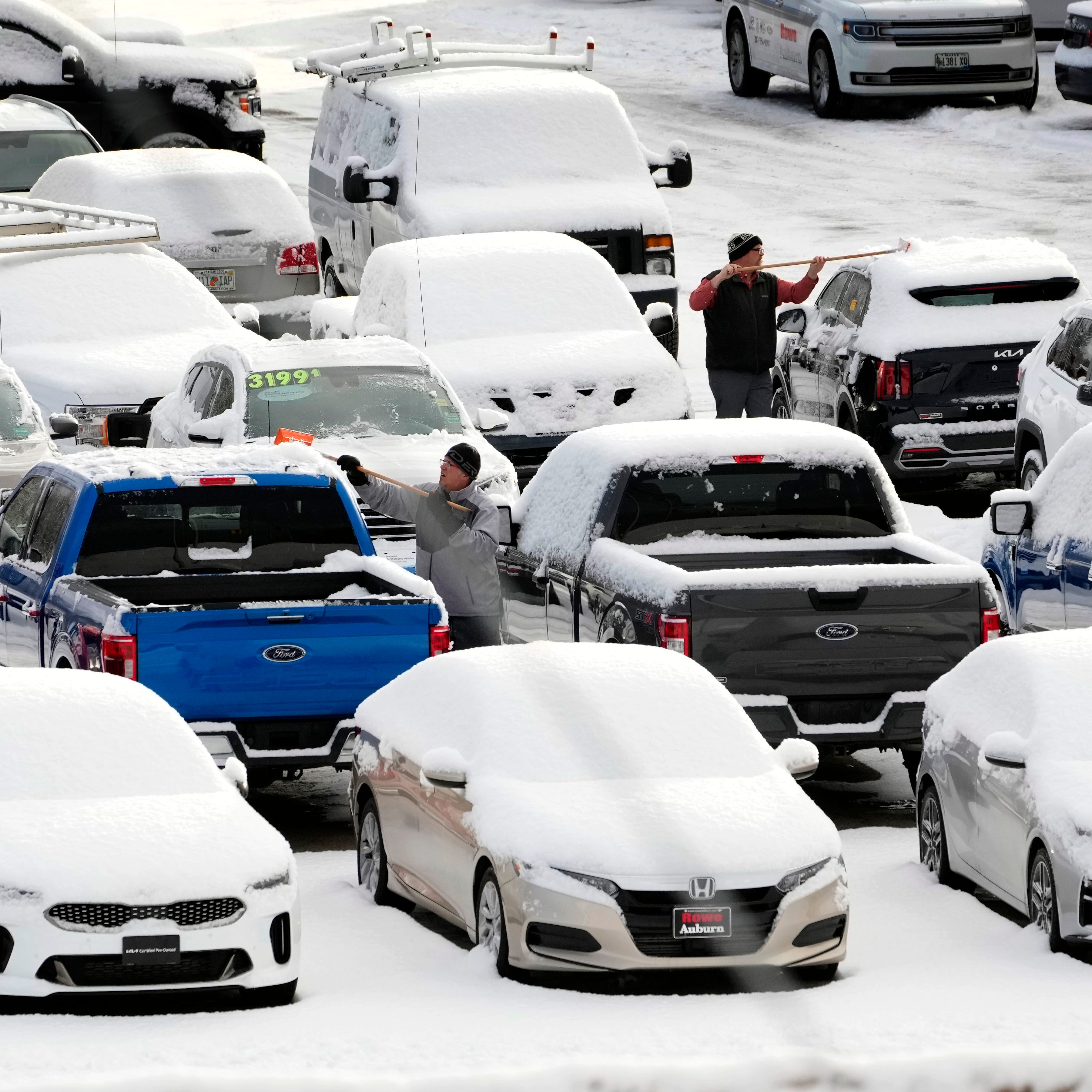 Workers at a Ford dealership clear fresh snow from vehicles in the used car lot, Tuesday, Jan. 31, 2023, in Auburn, Maine.