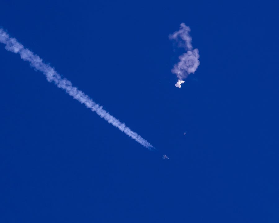 In this photo provided by Chad Fish, the remnants of a large balloon drift above the Atlantic Ocean, just off the coast of South Carolina, with a fighter jet and its contrail seen below it, Saturday, Feb. 4, 2023. The downing of the suspected Chinese spy balloon by a missile from an F-22 fighter jet created a spectacle over one of the state's tourism hubs and drew crowds reacting with a mixture of bewildered gazing, distress and cheering.