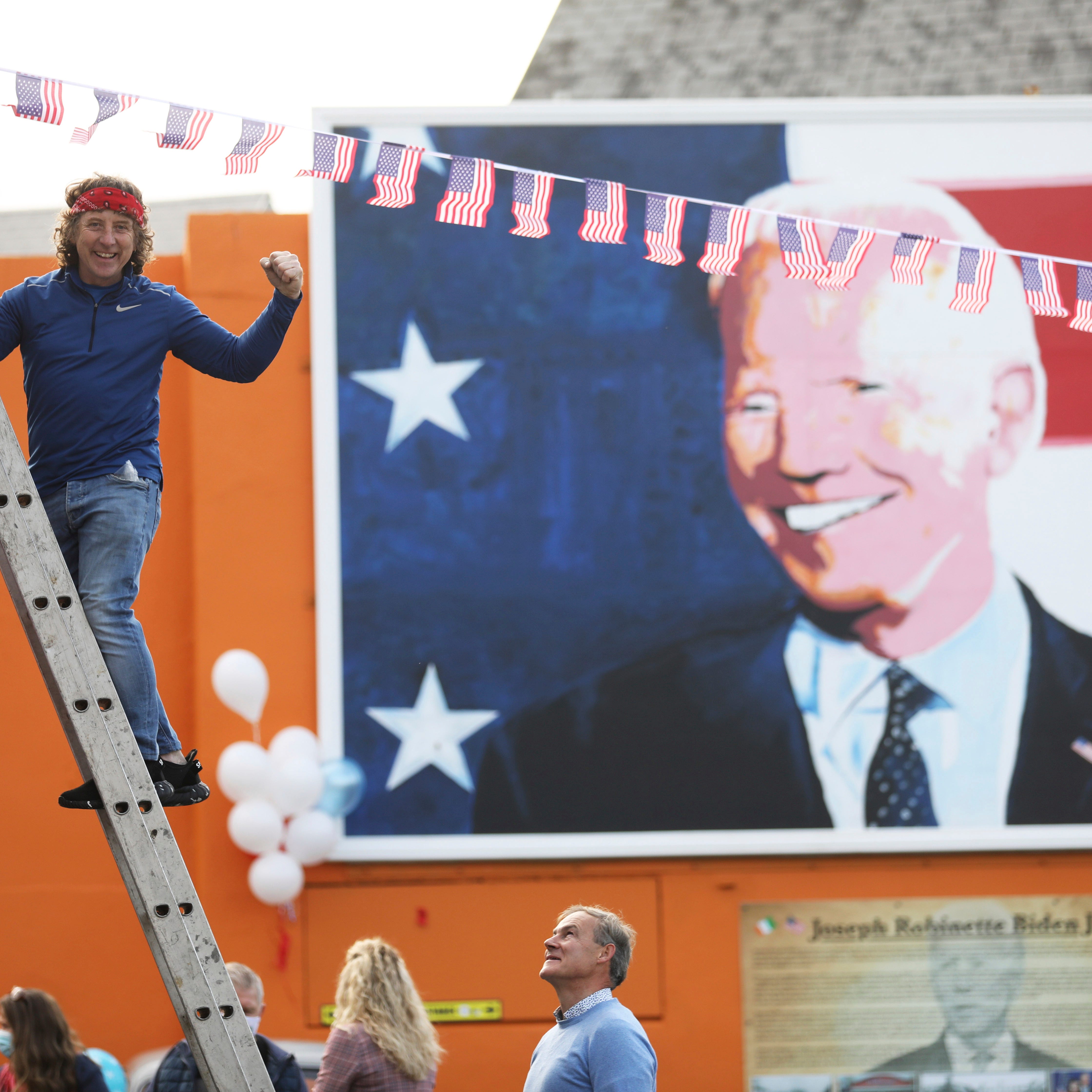 A man puts a US flag up in the town of Ballina, the ancestral home of President elect Joe Biden, in North West of Ireland, Saturday, Nov. 7, 2020. Biden was elected Saturday as the 46th president of the United States, defeating President Donald Trump in an election that played out against the backdrop of a pandemic, its economic fallout and a national reckoning on racism.  (AP Photo/Peter Morrison) ORG XMIT: XPM120