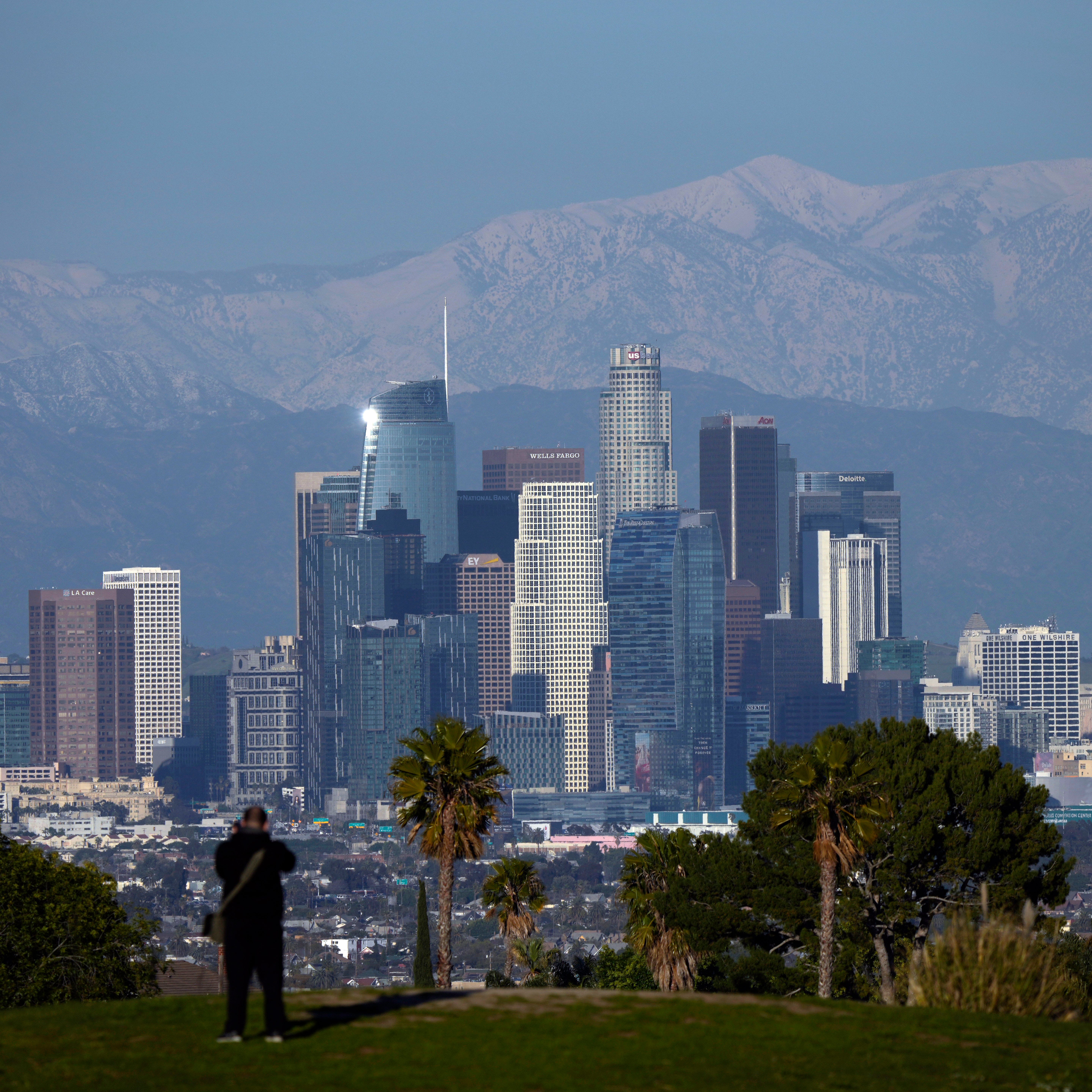 A visitor takes in a view of the city's skyline under the snow-covered San Gabriel mountains after a series of storms Thursday, March 2, 2023, in Los Angeles. (AP Photo/Marcio Jose Sanchez)