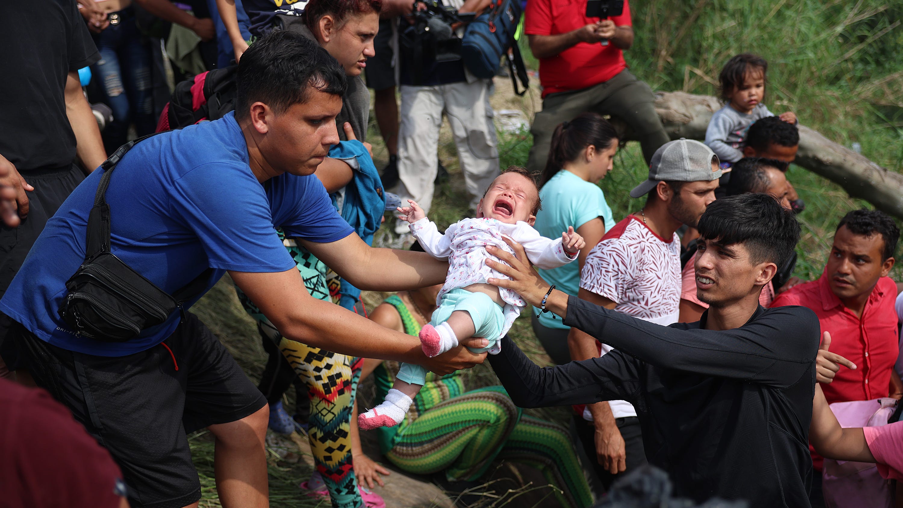 A baby is passed between people as migrants make their way into the Rio Grande as they cross to enter the United States on May 11, 2023 in Matamoros, Mexico.