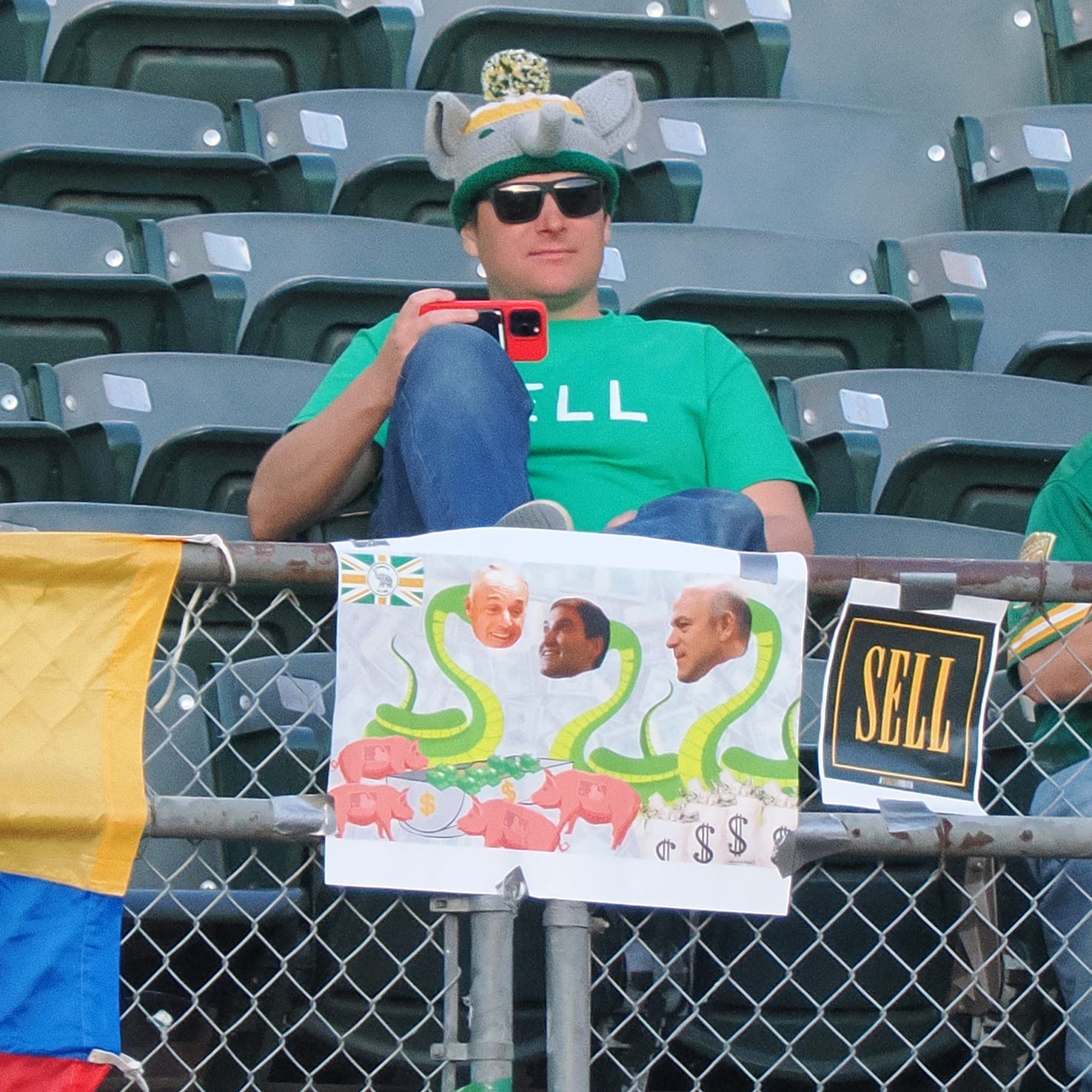 A sign with the faces of MLB commissioner Rob Manfred, Oakland Athletics president Dave Kaval and owner John Fisher (pasted onto the bodies of snakes above pigs with MLB logos, next to a sign reading 