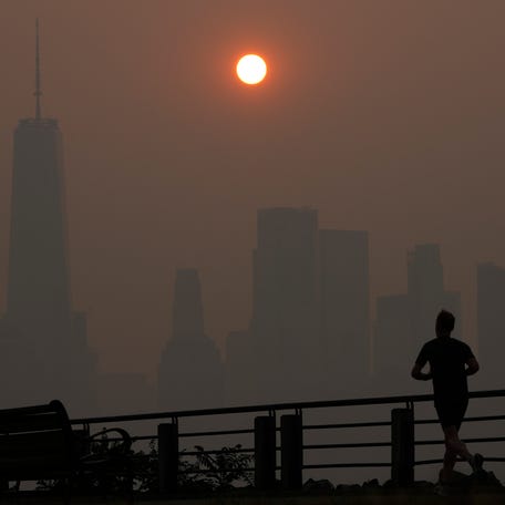 A man runs in front of the sun rising over the lower Manhattan skyline in Jersey City, N.J., June 8, 2023. Thick, smoky air from Canadian wildfires made for days of misery in New York City and across the U.S. Northeast this week.
